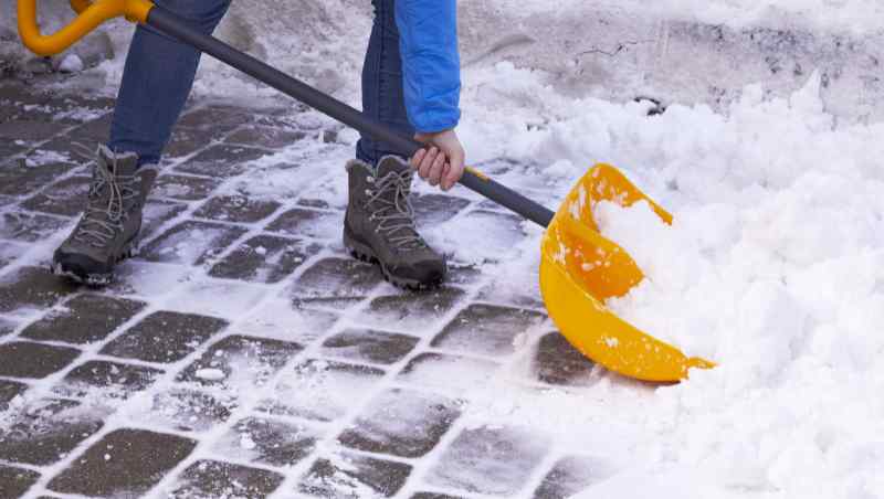 Man removing snow from pavers with a large plastic shovel