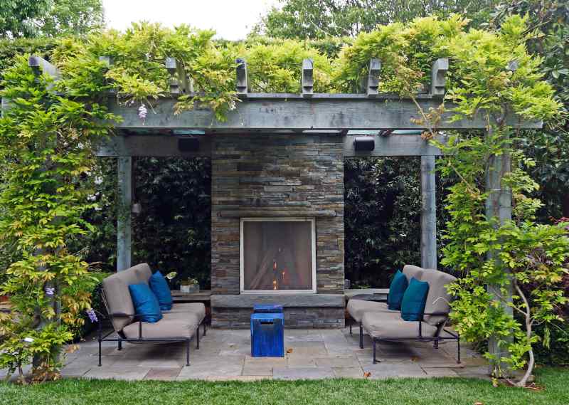A natural stone outdoor patio fireplace for lounging, covered with a pergola.