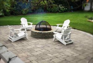 Four chairs on a landscaped patio around a backyard fire pit on a summer evening.