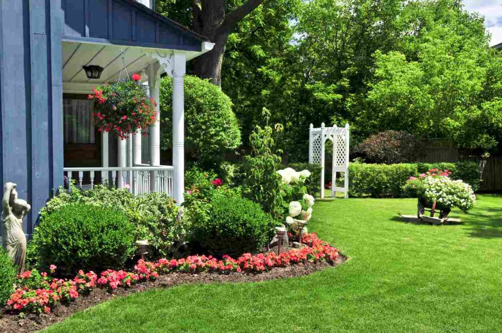 Landscaped front yard of a house with green grass and beautiful pink flowers done by professional area landscapers.