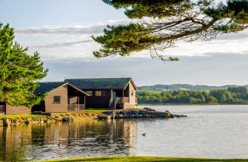 A peaceful scene of wooden lodges off a lake sitting on landscaping for a lake house